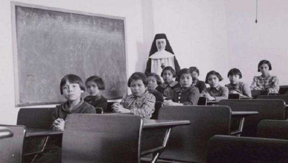 A group of female students and a nun pose in a classroom at Cross Lake Indian Residential School in Cross Lake, Mba., in a February, 1940. | Photo: Reuters 