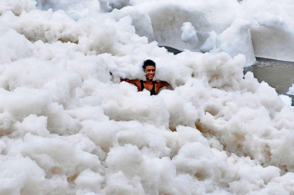 A man immerses himself in a large amount of toxic foam formed along the banks of the Yamuna on July 12, 2015, in Noida, India. The pollution is caused in part to high ammonia levels emanating from the high discharge of industrial pollutants in the river. 