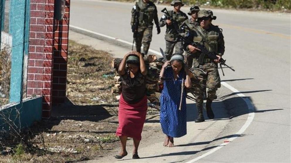 Indigenous women carry firewood on their backs and a group of soldiers walk near Yalambojoch, home village of eight-year-old migrant Felipe Gomez, who died in a medical center in Alamogordo, New Mexico, United States, on December 24, while in custody of U