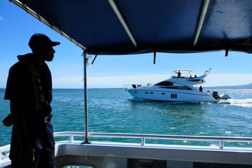 A crew member of police boat Veiqaravi watches a pleasure craft motor past in Nadi Bay.