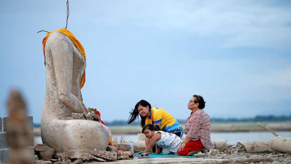 A family prays near the ruins of a headless Buddha statue that resurfaced in a dried-up dam because of a drought in Lopburi, Thailand, on Aug. 1, 2019. (Credit: Soe Zeya Tun/Reuters/Newscom)