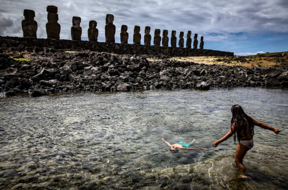 Children play in the ocean behind Ahu Tongariki on Easter Island. Credit...Josh Haner/The New York Times