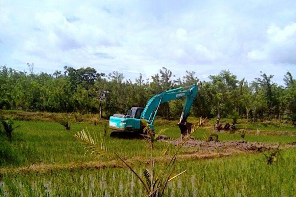 A bulldozer clears a path through rice paddies in Maroangin.