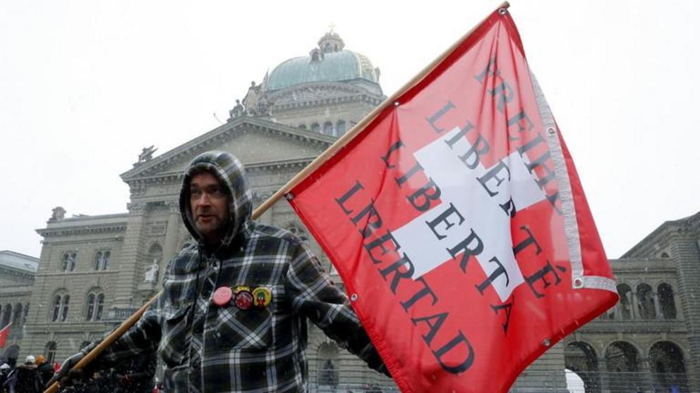 An anti-lockdown demonstrator holds a Swiss flag with the word 