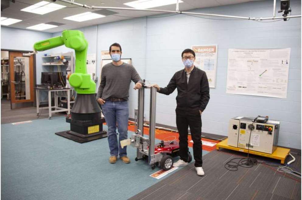 UC engineering students Sam King, left, and Yufeng Sun stand next to the autonomous robot they are building. Sun developed a successful AI that could find and open doors. Now he is translating his simulation to real-world hardware.