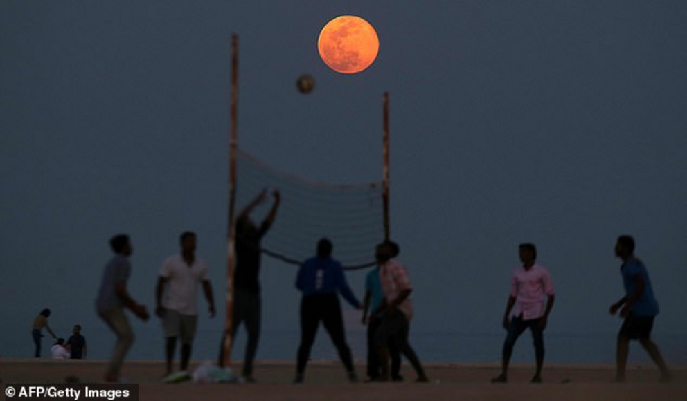 On Monday, the moon will appear full for nearly three days around the same time, 11:32pm ET, starting Sunday through Wednesday morning. But it will glow in its full brilliance Monday evening. People play volleyball on the beach as the Pink Moon rises in t