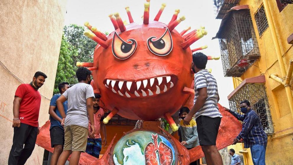 FILE PHOTO. People are seen near a giant effigy resembling the Covid-19 coronavirus. © AFP / SUJIT JAISWAL
