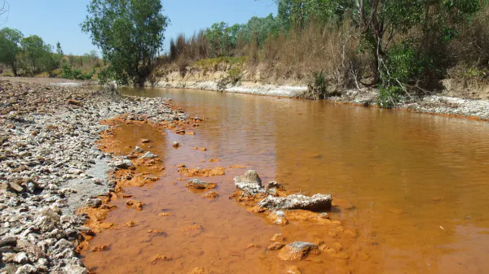 The iron-tainted red hues of the Finniss River near the waste rock dumps leaking acid mine drainage.