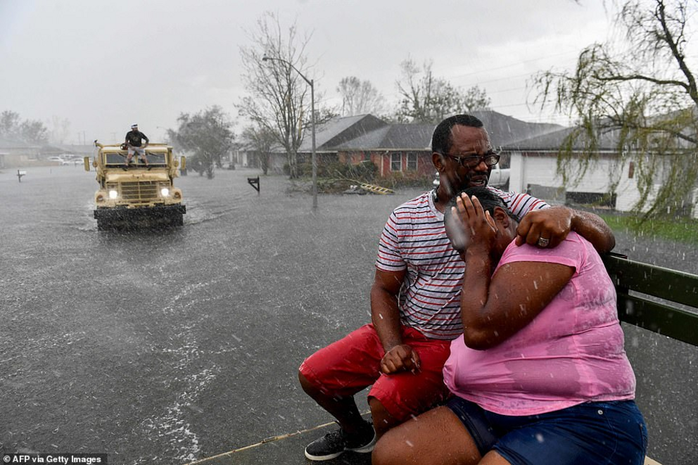 People react as a sudden rain shower soaks them with water while riding out of a flooded neighborhood in a volunteer high water truck assisting people evacuating from homes after neighborhoods flooded in LaPlace, Louisiana