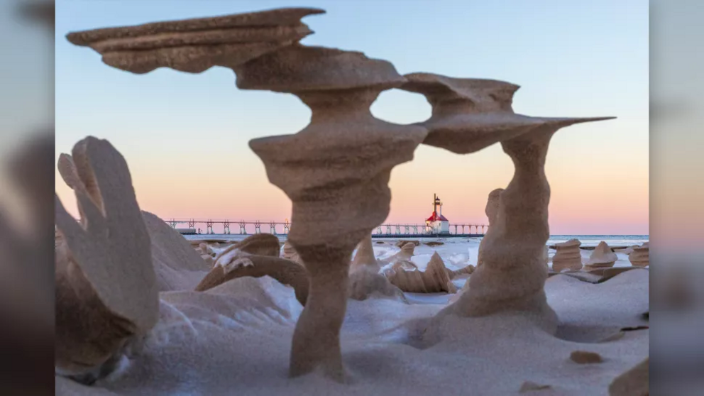 A view of the North Pier Lighthouse through the sand pillars on the beach by Lake Michigan.