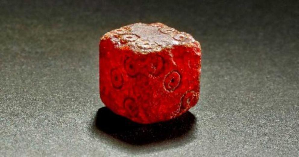 An amber die, from 1st or 2nd century Rome, with the numbers arranged so that opposite sides add up to seven; the units are marked by a dot within a circle.
