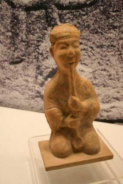 A Chinese Eastern Han Dynasty (25-220 AD) ceramic figurine of a musician playing a xiao flute, from the Pengshan Tomb of Sichuan.