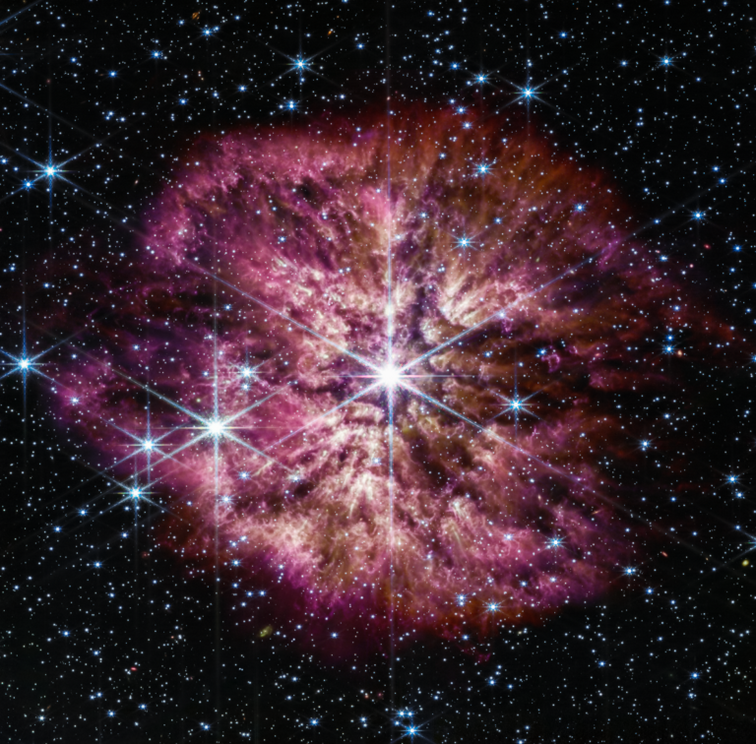 The luminous, hot star Wolf-Rayet 124 (WR 124) is prominent at the center of the James Webb Space Telescope’s composite image combining near-infrared and mid-infrared wavelengths of light from Webb’s Near-Infrared Camera and Mid-Infrared Instrument.